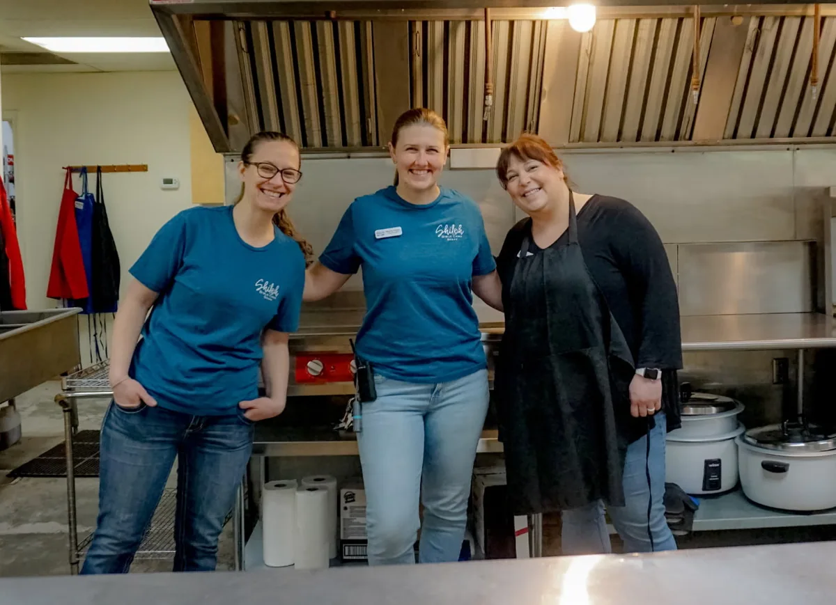 Three women smiling together in the camp kitchen