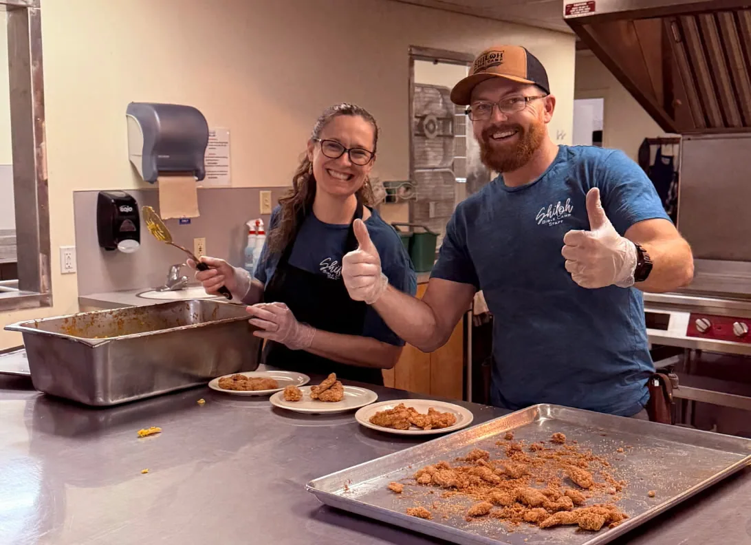 Chase and Stephanie smiling while serving food in the camp kitchen